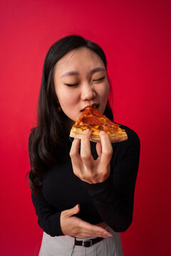 Cheerful Asian woman biting pizza
