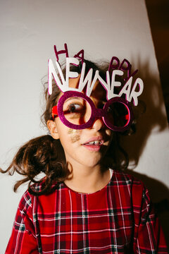 Kid making funny faces with Happy New Year party glasses. Direct flash