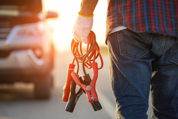 Man holding red and black battery cable for charging the car. Car Repair and maintenance concept - obrazy, fototapety, plakaty
