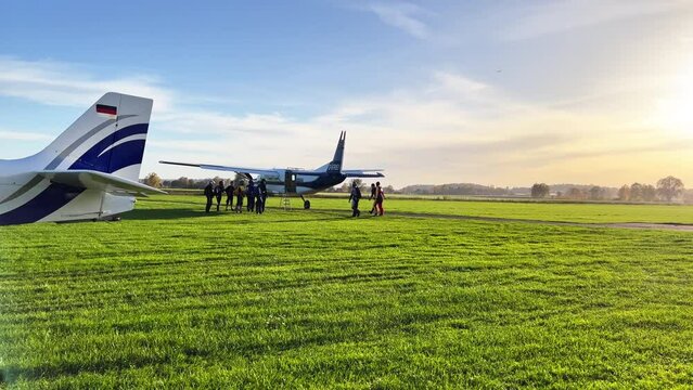 Wide shot of a few parachuters getting ready and walking to the plane on the ground. Group of people standing already near the plane.  Static camera, nice afternoon sun.