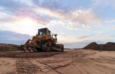 The yellow bulldozer stands on the ground. Against the background of the sunset sky