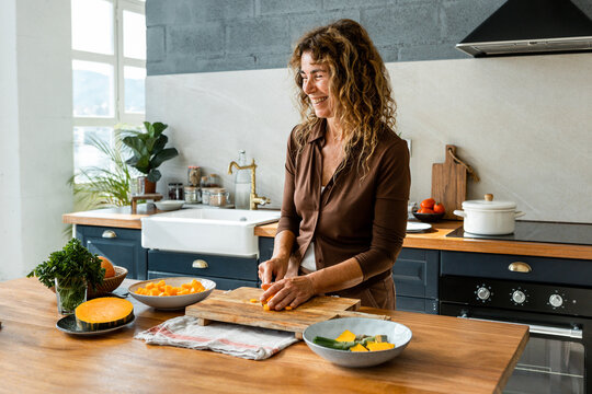 senior woman with curly hair smiles while preparing a recipe