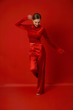A woman in a red fashionable outfit dances on a red background