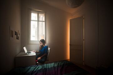 Smiling woman using laptop in dark bedroom