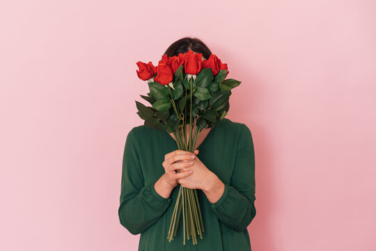 Lady with bouquet of red roses against pink background.