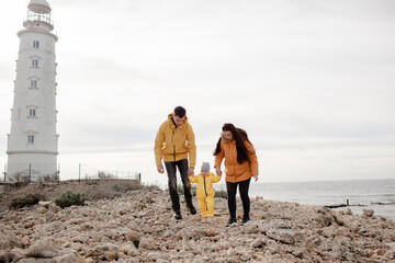 Happy multinational family walking in the beach with little kid tigether in cold weather against the background sea