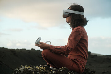 Woman with VR glasses and joysticks sitting outdoors