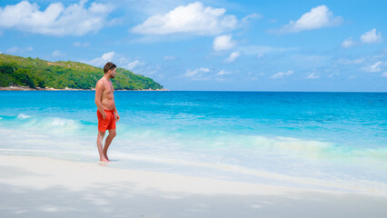 Young men in a swim short relaxing at Anse Lazio beach with turquoise colored ocean Praslin Seychelles Islands.