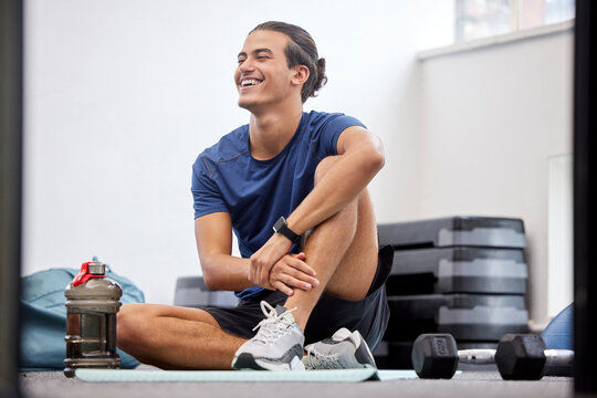 Fitness, relax or happy sports man at gym after training, workout or exercise resting on a break. Tired, smile or healthy athlete with fatigue relaxing on a mat alone after exercising for body goals