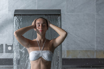 Young woman washing hair under shower in spa
