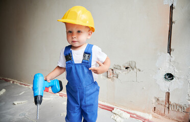 Child with toy construction tool for repair works standing against the wall in apartment under...