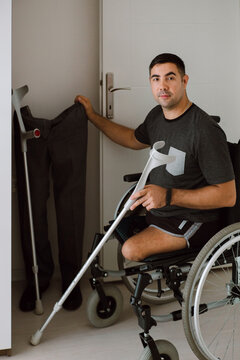 Man in a wheelchair next to his prosthetic legs and crutches 