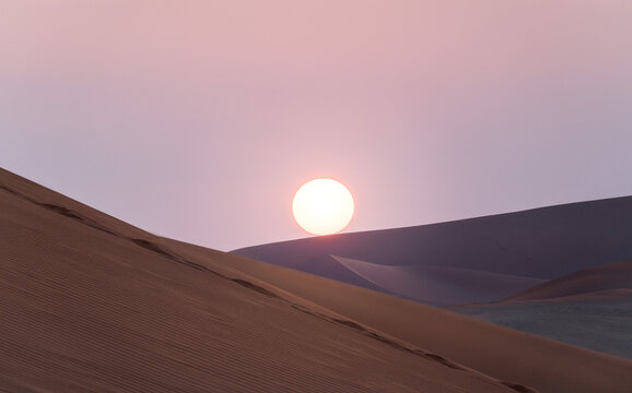 Sand dunes in front of the sun at sunset in Namibia, Africa.