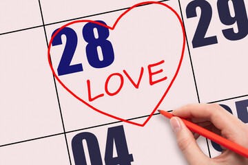 28th day of the month. Hand writing text LOVE and drawing a red heart on a pink calendar date.