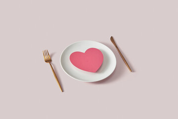 Pink heart on white plate with fork and knife.