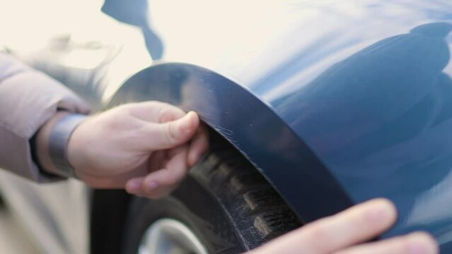 A close-up shot of a male hands, as he examines a scratch on his car,