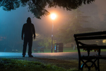 A hooded figure silhouetted in a park at night