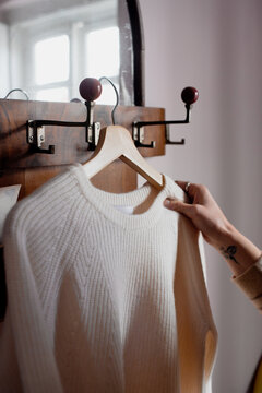 Hand touching a jumper on a wood hanger