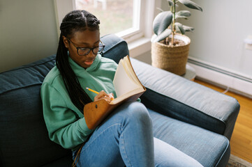 black teenage girl sitting down writing in a journal