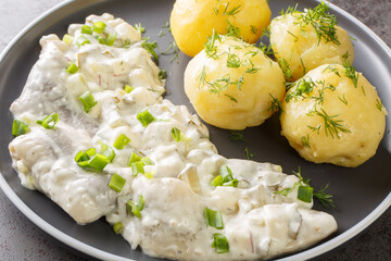 Spicy herring fillet in a creamy sauce with a garnish of boiled potatoes close-up in a plate on the...