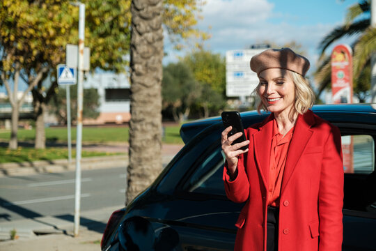 Woman browsing phone while recharging electric car 