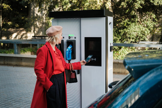 Woman paying with phone at electric recharging Station