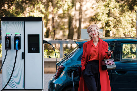 Woman looking at camera while recharging electric car 