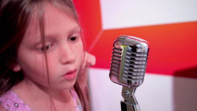 Junior Schoolgirl Makes Sounds Moving Away And Moving Closer To Microphone. Child Listens To Own Voice Carefully On Blurred Background Closeup