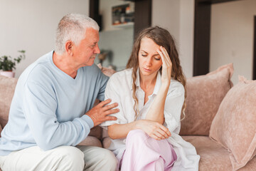 Worried aged father embracing comforting sad grown up daughter with broken heart family sit on sofa