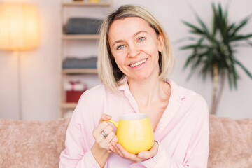 Adult woman sitting on the sofa at home and having a cup of coffee