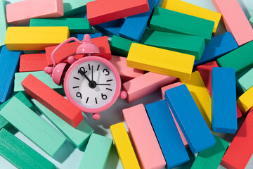 Block tower made of colourfull wooden blocks on light blue background and a clock