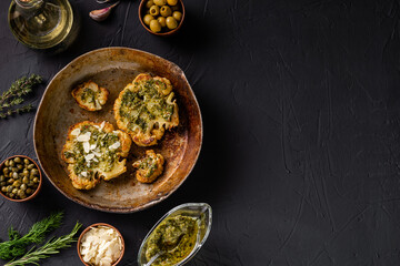 Cauliflower steak with spices, chimichurri sauce, almond flakes. Capers, olives, herbs, side by side. Dark background. Vegetarian food. Copyspace.