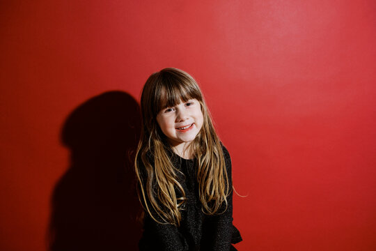 classic flashy portrait of smiling toddler girl in front of red wall