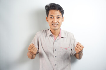 excited Asian man celebrating success with two fists in air isolated on the blue background. close up portrait, studio shot , happiness, positive emotion and feeling. I've done it. facial expression