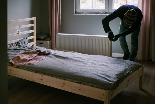 Adult man unpacking new heating radiator next to wooden bed 