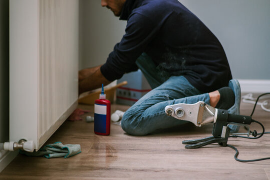 Male worker uses PVC Pipe welding machine near heating radiator