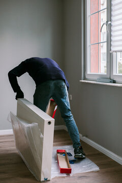 Adult man unpacking new heating radiator next to the window. 