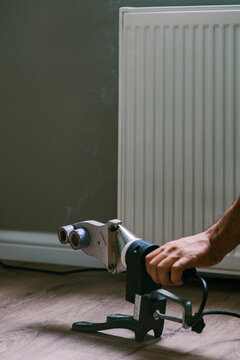 Male worker uses PVC Pipe welding machine near heating radiator