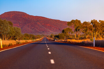 Fototapeta na wymiar sunrise in karijini national park in western australia; a road through the australian outback with red rocks and mountains in the background