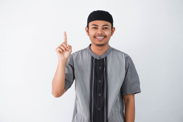 young asian muslim man finger pointing up raising a finger got a good idea looks surprised with a smile wearing grey koko clothes, isolated on a white background.