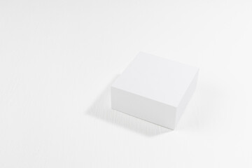 Fashion contemporary scene - white square podium mockup in hard light with shadow on soft light white wood background, top view, template for presentation cosmetic products, goods, branding, design.