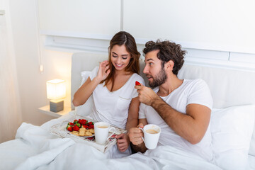 Obraz na płótnie Canvas Young married couple in love eating breakfast in their bed. Good morning! Healthy breakfast in bed. Young beautiful love couple is having breakfast in bed.
