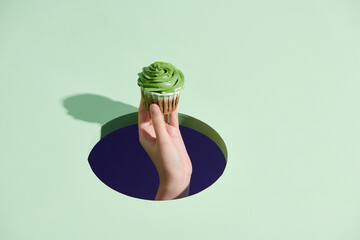 cropped view of woman holding tasty cupcake on green