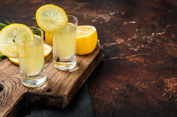 Italian limoncello liqueur and fresh lemons on a rustic wooden board. Dark background. Top view....