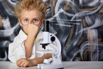 A boy in the form of a scientist in a white coat adjusts round glasses. A cute child is studying...