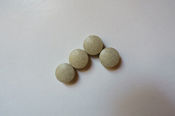 Group of four beige round pills of iron bisglycinate dietary supplement from above