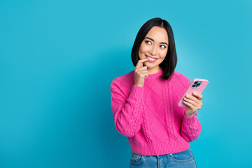 Portrait of pretty cute indonesian girl finger touch lip hold telephone look empty space isolated on blue color background