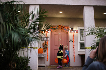 Rear view of siblings wearing costumes while trick or treating on porch during Halloween