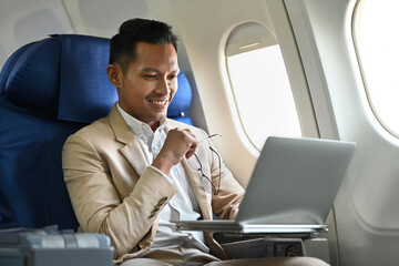 Successful businessman in elegant luxury suit working with laptop in aircraft during business travel