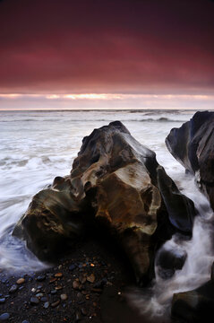 Waves crashing over a beach boulder on Ruby Beach in Olympic National Park at sunset.